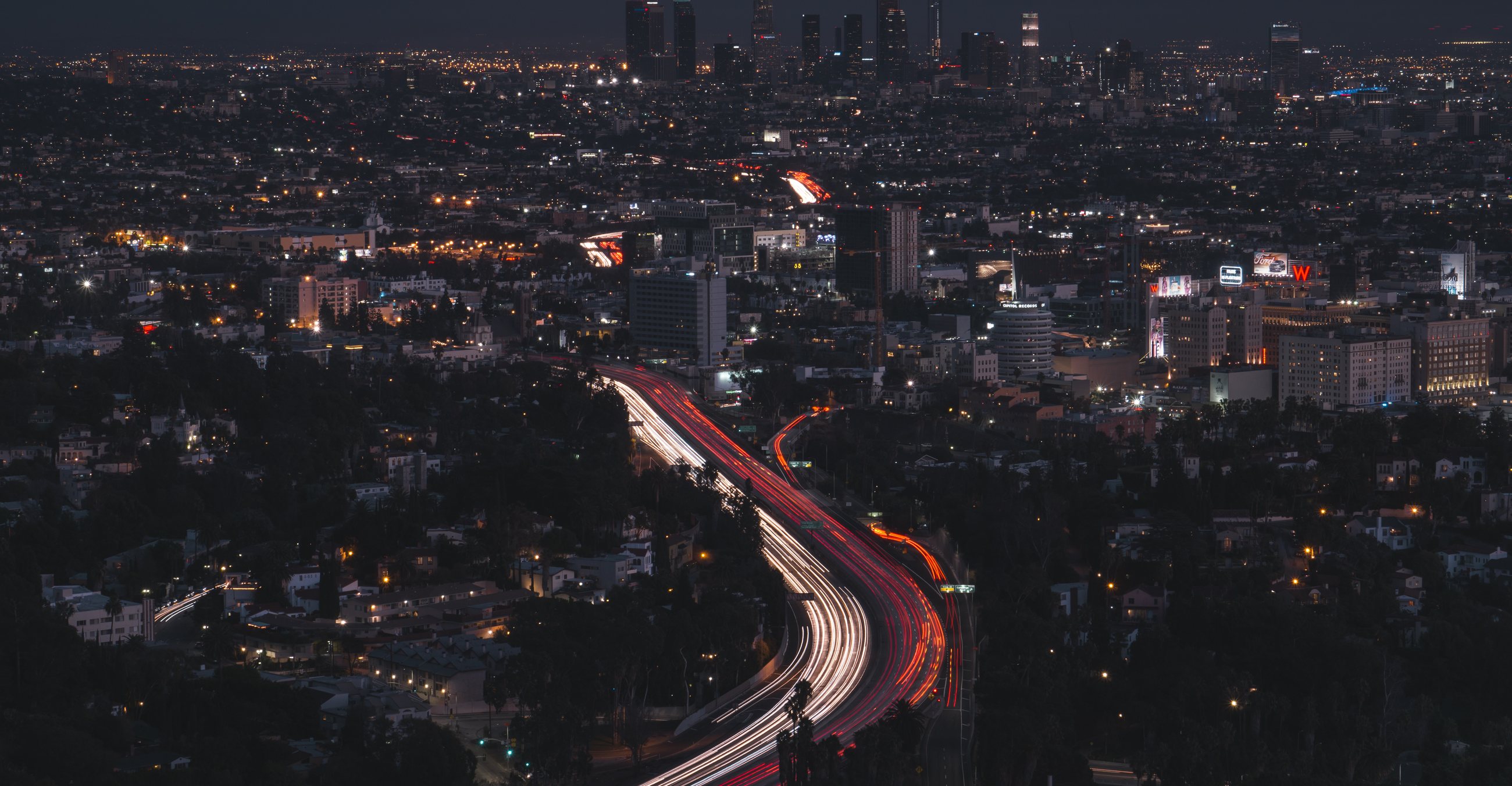 Freeway light trails running toward the downtown Los Angeles skyline at night